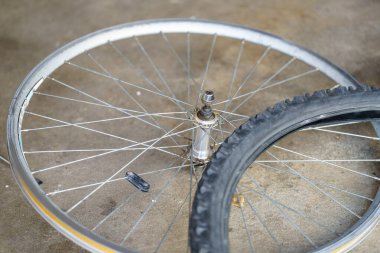 Lastiği kısmen sökülmüş bir bisiklet tekerleği yerde yatıyor. Biri daireyi tamir etmeye hazırlanırken ve yola koyulurken, hayat boyunca bisiklet sürerken, ışıklar parlıyor..