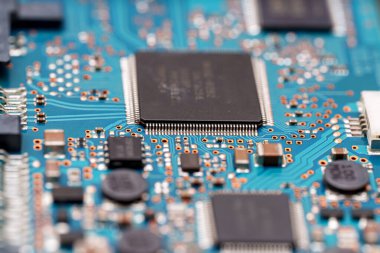 Yakın çekim, entegre çipler ve çeşitli bileşenlerle dolu canlı bir mavi devre kartı sunar. Elektrik yolları karmaşık bağlantılar örüyor, sistemin süreçlerini destekliyor.