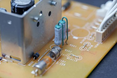 Sarımsı baskılı devre kartındaki elektronik bileşenleri yakından izle. Bir sigorta, kondansatörler, rezistörler ve konnektörler açıkça görülüyor..