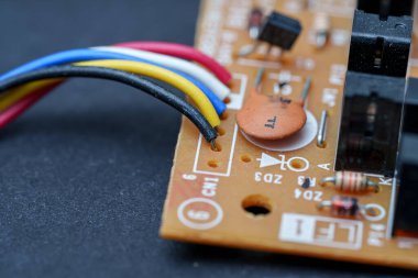 Detaylı bir yakın çekim bir devre kartına lehimlenmiş kabloları gösteriyor. Direnç ve kondansatör gibi çeşitli elektronik bileşenler görülebilir. Sahne kesinliği vurgular..