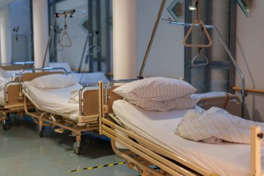 Bir hastane koridorunda, birkaç boş hasta yatağı düzgünce düzenlenir. Her yatağın beyaz çarşafları ve yastıkları var. Gün boyunca hastaların iyileşmesi için temiz ve düzenli bir yer sunuyorlar..