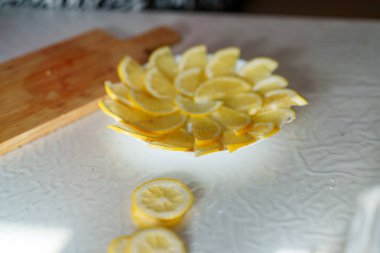 Taze limon dilimleri sanatsal olarak beyaz bir tabakta dairesel bir düzende düzenlenmiştir. Canlı sarı renklerini sergilerler..