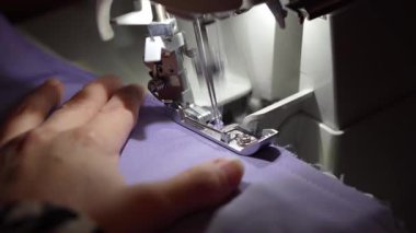 Bir insan lavanta renkli kumaşın kenarlarını düzgünce tamamlamak için serger dikiş makinesi kullanır. Profesyonel görünümlü bir kenar oluşturur. El işleri ve giysi yapımında harikadır.!