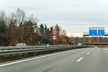 Parçalı bulutlu bir günde, Autobahn 'da seyahat eden bir arabadan dışarı bakılır. Hız limiti var ve Deutschland 'da yol kenarında sollama işareti yok..