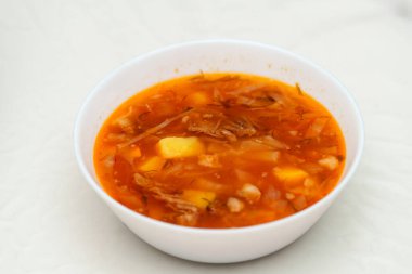 Klasik bir Doğu Avrupa çorbası olan dumanı tüten bir tas Borscht parlak bir masada oturur. Patates ve parçalanmış lahana parçaları zengin, kırmızımsı et suyunda görülebilir..