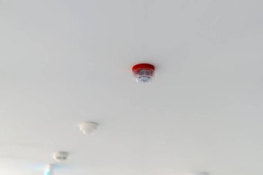 Pürüzsüz beyaz bir tavana bağlı kırmızı yangın alarmı. Ek duman dedektörleri yakına yerleştirilerek binada bir yangın güvenliği ağı oluşturuldu..