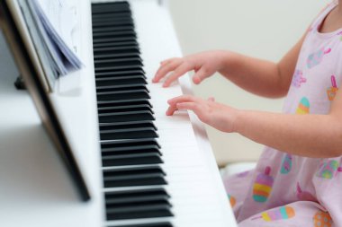 Yazlık elbiseli küçük bir çocuk beyaz bir piyanoda şarkı çalar. Küçük eller notaların rehberliğinde tuşlara basar. Parlak bir günde müzik yapmayı öğrenirler..