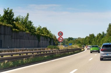 Araçlar asfalt karayolu boyunca yeşil ağaçlar ve yol kenarında beton bir duvar ile hareket ediyor. İmza, otobanın bu bölümünde kamyonun hızını 120 km 'ye düşürür..