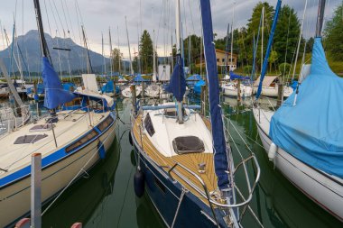 Birçok yelkenli Starnberger See, Almanya 'da bir limanda demirlemiş durumda. Alpler bulutlu gökyüzünün altında yükselerek manzaralı ve huzurlu bir deniz manzarası yaratıyorlar..