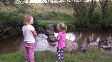 İki çocuk taşlı küçük bir su kütlesinin yanında. Günlük giysiler giyiyorlar ve güneşli bir öğleden sonranın tadını çıkarıyor gibi görünüyorlar..