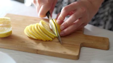 Birisi parlak sarı bir limonu ahşap bir kesme tahtasının ince dilimlerine ayırıp parlak bir mutfakta aşçılık için hazırlıyor..