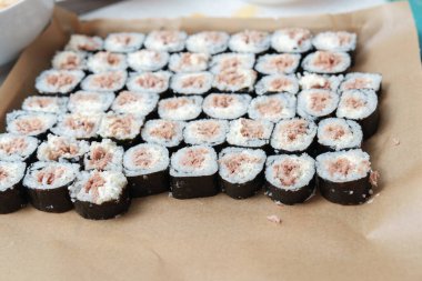 Ton balığı ve pirinçle doldurulmuş taze yapılmış suşi ruloları düzgünce dizilmiş bir tepsi. Lezzetli bir atıştırmalık için servis edilmeye hazırlar..