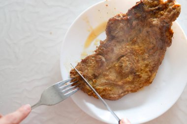 Buharda pişmiş, kahverengi fileto bifteği titizlikle beyaz bir tabakta çatal ve bıçakla kesiliyor, tadını çıkarmaya hazır. Sahne temiz ve davetkar..