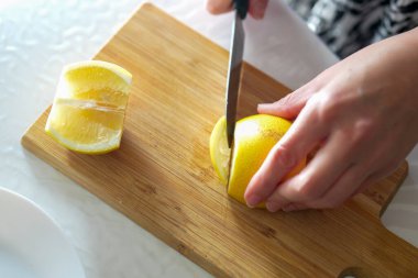 Bir aşçı zarif bir şekilde parlak sarı bir limonu, sağlam bir kesme tahtasının üzerinde ışıldayan bir bıçakla dilimliyor ve lezzetli bir yemek tarifine hazırlanıyor..