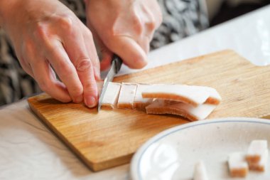 Bir kişi yemek hazırlıyor. Elleri, bir parça domuzu odun kesme tahtasıyla küçük parçalara ayırırken gösteriliyor. Yakınlarda bir tabak var..