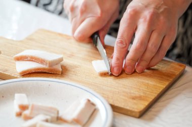 Eller ustalıkla, ahşap bir kesme tahtasının üzerinde beyaz, buzlu bir ziyafeti kesiyor, benzer kesiklerle dolu bir tabağın yanında, bu da mutfak yaratımı için bir hazırlık olduğunu gösteriyor..