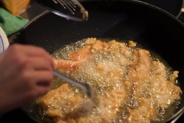 Yiyecek, siyah bir tavanın içinde kaynayan yağda cızırdıyor. Bir insan, mutfakta çıtır çıtır bir şaheser yaratmak için mutfak aletlerini kullanır..