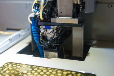 Bir makine üretim sahasında çalışıyor. Çeşitli bileşenleri birleştirmeye ve işlemeye odaklanır. Cihazlar ve kablolar makinelerin etrafında düzenlenir.