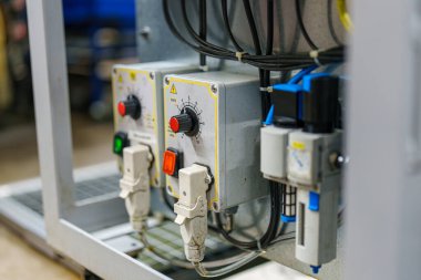 Çeşitli düğmeler ve göstergelerle bir kontrol paneli gösterilir. İşçiler gündüz saatlerinde atölyede makineleri yönetmek için kullanırlar. Çevre operasyonlara ve güvenliğe odaklanmış durumda.