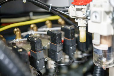 Bu, bir atölyedeki makinelere bağlı çeşitli elektrik bileşenlerini gösteriyor. Makineler kablolar, hortumlar ve çeşitli tesisatlarla çevrili..