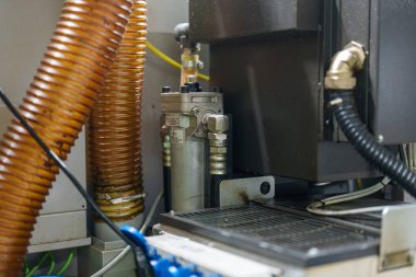 Teçhizat çeşitli borular ve filtrelerle bir atölye ortamında gösteriliyor. Bazı kablolar birbirine bağlıdır ve bakım faaliyetleri şu anda gerçekleşmektedir.