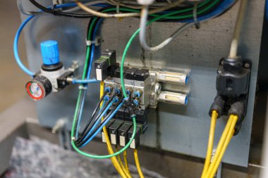 Endüstriyel bir makinenin kontrol paneline bağlı birkaç kablo var. Kurulum bir basınç göstergesi ve denetim işlemleri için çoklu elektrik bağlantılarını içerir.