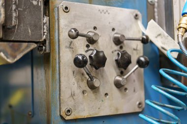 Panelde bir atölyede makineleri kontrol etmek için kullanılan birkaç düğme ve kol var. Panel mavi bir yüzeye monte edilir ve araçlar arka planda mevcuttur.