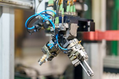 Bir robotik kol fabrikada çalışır. Çalışma saatlerinde birden fazla alet ve kabloyu yönetiyor, endüstriyel ortamda otomasyon sergiliyor.