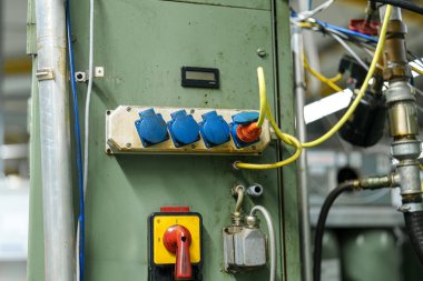 Bir kontrol paneli mavi şalter ve kablolarla görülebilir. Sarı ve kırmızı kablolar birbirine bağlı. Gündüz vakti imalat tesisi gibi görünüyor..