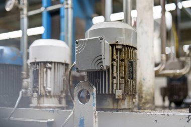 Fabrikada birkaç elektrik motoru gösteriliyor. Metal bir çerçeveye monte edilmişler ve kullanılmış görünüyorlar. Çevre çeşitli endüstriyel elementlerle meşgul görünüyor..