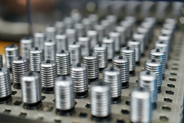 Sıralar halinde dizilmiş küçük metal bileşenler bir fabrikanın çalışma yüzeyinde düzgünce düzenlenir. İş yapılırken araçlar ve makineler arka planda görünür.