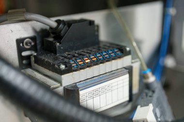 Bir kontrol paneli endüstriyel ortamdaki çeşitli düğmeleri ve kabloları gösteriyor. Ayar iyi ışıklandırılmış ve ekipmanlar çalışıyor gibi görünüyor..