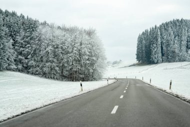 Sahne, karla kaplı, buzlu ağaçlar ve tepelerle kaplı dolambaçlı bir yolu gösteriyor. Kırsal kesimde sakin bir yerde sabahın erken saatleri..