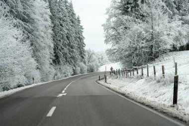 Her iki tarafında karla kaplı ağaçlar olan bir kış sahnesinde yol kıvrılır. Bulutlar ve karlı koşullar nedeniyle düşük görüş mevcuttur.