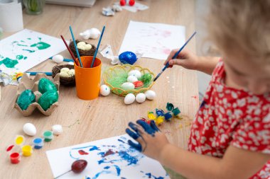 Genç bir kız Paskalya yumurtalarını boyayarak eğleniyor ve paskalya bayramı için mavi boya ile el izi sanatları yapıyor..