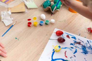 Çocuk masaya renkli boya ile yumurta boyuyor, bayram için paskalya yumurtalarını süslüyor ve kağıt üzerinde renkli tasarımlar yapıyor. Neşeli, neşeli bir etkinlik..