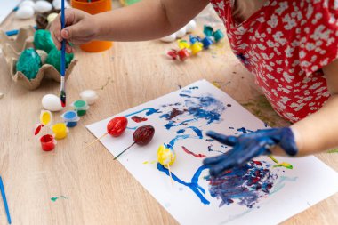 Bir çocuk Paskalya yumurtalarını süslüyor ve canlı resimlerle kağıt üzerinde sanat eserleri yaratıyor. Etkinlik kapalı bir masada gerçekleşiyor. Paskalya tatili için neşeli ve yaratıcı bir ifade..