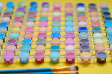 Çeşitli renklerde küçük boya kapları düzgünce bir masanın üzerine yerleştiriliyor. Yanında kullanılmaya hazır iki boya fırçası var. Bu ayar sanat için araçları gösterir.