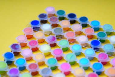 Birçok küçük konteynır parlak sarı bir yüzey üzerinde düzgünce düzenlenmiş farklı renkte boya içerir. Bu düzen sanat projeleri ve el sanatları için idealdir, yaratıcılığı ve eğlenceyi teşvik eder..