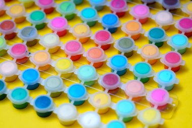 Parlak sarı bir masaya boya dolu küçük kaplar konur. Her kap sanat ve zanaat projelerinde kullanılmaya hazır parlak renkler gösteriyor. Bu ortam yaratıcı işler için idealdir..