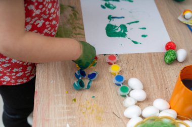 Küçük kız masada paskalya yumurtası yapıyor.