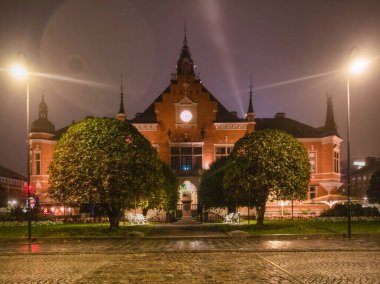 Umea Radhus (Umea belediye binası) geceleri ıslak kaldırım taşı meydanı ve parlayan sokak lambalarıyla aydınlanıyor..