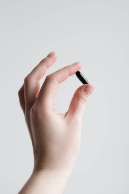 Beyaz arka planda tek bir demir kapsülü tutan bir elin yakın çekimi, ferritini, demir takviyesini, anemi önlemeyi ve sağlıklı yaşam tarzını simgeliyor, tıbbi ve sağlıklı kullanım için ideal.