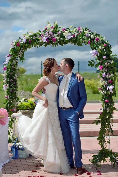 Hermosa novia con novio cerca del arco de la boda — Foto de Stock