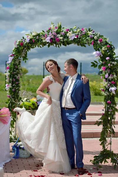 Hermosa novia con novio cerca del arco de la boda — Foto de Stock