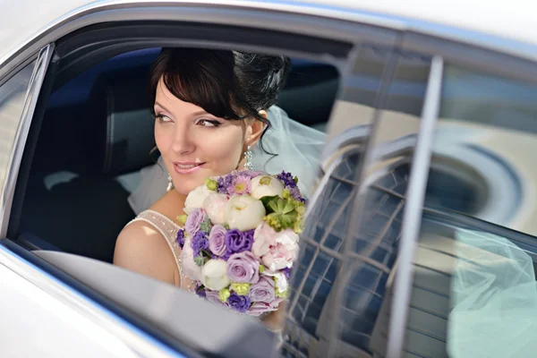 Bruid met boeket en kantpatroon sluier in auto — Stockfoto