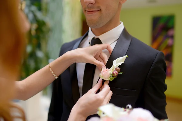 Bruden bär boutonniere på brudgummen — Stockfoto