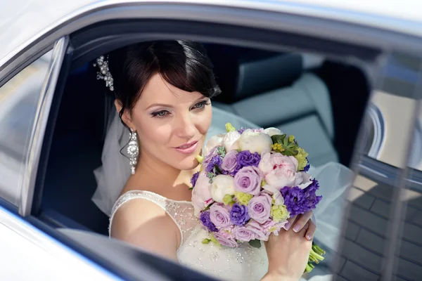 Bruid met boeket en kantpatroon sluier in auto — Stockfoto