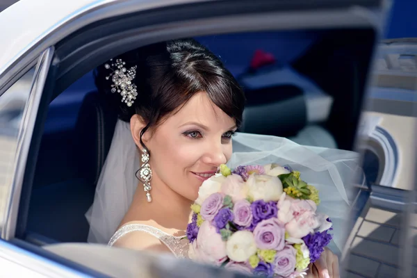 Bride with bouquet and lace veil in car — Stock Photo, Image