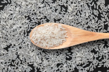 Siyah arka planda tahta kaşıkta pirinç.